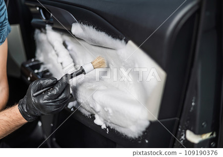 A man cleans the interior of a car with foam and a brush. Clean the door trim. 109190376