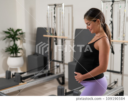 Beautiful pregnant woman stands in a yoga studio and gently touches her belly. Beautiful pregnant woman stands in a yoga studio and gently touches her belly. 109190384