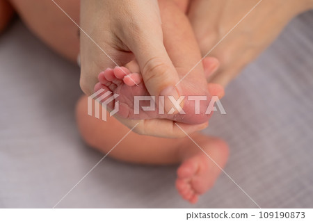 A young mother holds the foot of her newborn son with a bruise from neonotal screening. Close-up of woman's hands. A young mother holds the foot of her newborn son with a bruise from neonotal screening. Close-up of woman's hands. 109190873