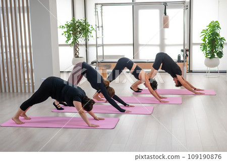 Three women and a man stand in the Downward Facing Dog pose. Group of people doing yoga.  109190876