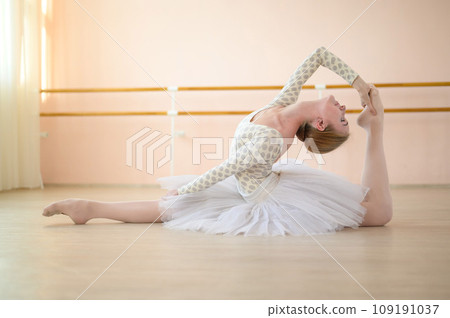 Beautiful ballerina in body and white tutu is training in a dance class. Young flexible dancer posing in pointe shoes sitting on the floor. Beautiful ballerina in body and white tutu is training in a dance class. Young flexible dancer posing in pointe shoes sitting on the floor. 109191037