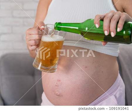 Faceless pregnant woman pouring beer into a glass.  109191041
