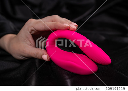 A woman holds a pink curved vibrator while lying on a black silk sheet. A woman holds a pink curved vibrator while lying on a black silk sheet. 109191219