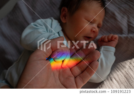 A man holds his newborn son's hand. Beam of light through a prism. A man holds his newborn son's hand. Beam of light through a prism. 109191223
