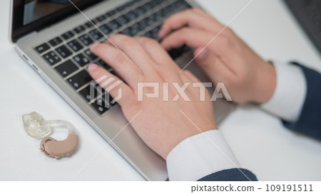 Close-up of a man's hands on a laptop keyboard. Hearing aid on the desktop. Close-up of a man's hands on a laptop keyboard. Hearing aid on the desktop. 109191511