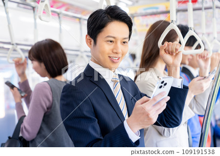 一位中年商人在上下班時看著智慧型手機。照片由京王電鐵株式會社提供。 一位中年商人在上下班時看著智慧型手機。照片由京王電鐵株式會社提供。 109191538