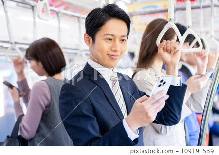 A middle-aged businessman looking at his smartphone while commuting. Photo provided by Keio Electric Railway Co., Ltd. A middle-aged businessman looking at his smartphone while commuting. Photo provided by Keio Electric Railway Co., Ltd. 109191539