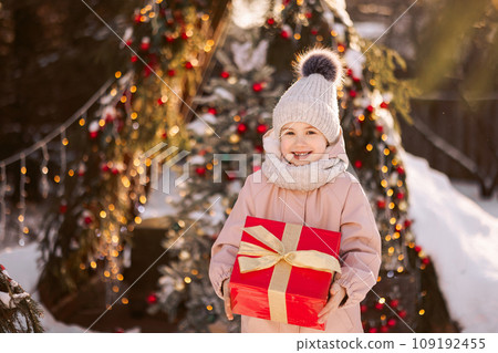 Little girl with a Christmas gift outdoors in winter on Christmas Eve. 109192455