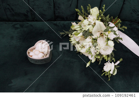 Box with rings in the shape of a heart and a wedding bouquet of roses on a green background 109192461