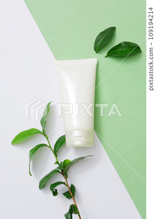 The background is divided into two minimalist colors with an unbranded cream tube and green tea leaves. Blank labels for cosmetic branding. Copy space for ads. 109194214