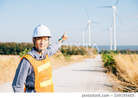 Technician helmet-clad engineer at windmill farm. Ensuring clean energy an Asian expert checks turbine efficiency. Innovating for global electric security dedication and expertise portrayed. Technician helmet-clad engineer at windmill farm. Ensuring clean energy an Asian expert checks turbine efficiency. Innovating for global electric security dedication and expertise portrayed. 109195605