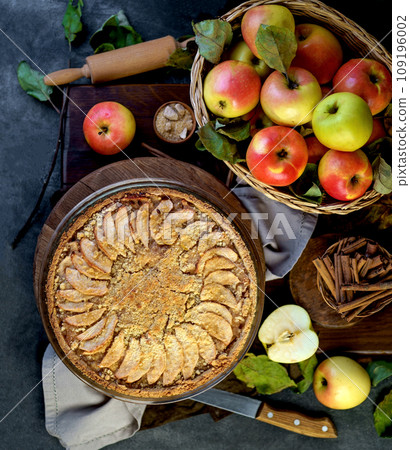 Apples and cinnamon are used in baking. Homemade apple pie on dark rustic background, top view. Classic autumn dessert Apples and cinnamon are used in baking. Homemade apple pie on dark rustic background, top view. Classic autumn dessert 109196002