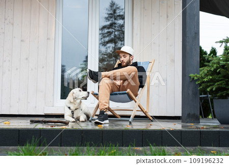A young man rests near his country house with a dog. 109196232