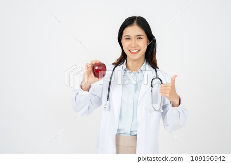 Female doctor with a white coat smiling and holding an apple. 109196942