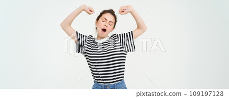 Portrait of tired girl yawning and stretching her arms. Lazy woman looking sleepy, standing over white background 109197128