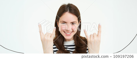 Close up portrait of excited young woman, rock n roll girl, showing heavy metal horn fingers and smiling, enjoys concert, having fun, standing isolated over white background 109197206