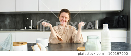 Attractive young cheerful girl baking at the kitchen, making dough, holding recipe book, having ideas Attractive young cheerful girl baking at the kitchen, making dough, holding recipe book, having ideas 109197990