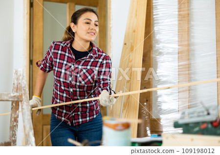 Woman carrying wooden planks, renovating apartment 109198012