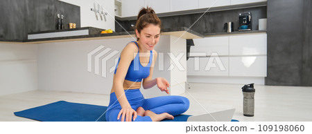 Portrait of fit, smiling fitness instructor, woman talking to laptop, discussing workout exercises with client, giving online yoga lesson via video chat 109198060