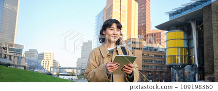 Happy young brunette girl, asian woman walks around city with tablet, goes to university with her digital gadget and backpack 109198360