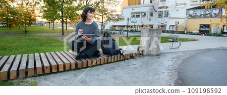 Young asian girl, student sits on bench, graphic designer with pencil and digital tablet draws scatches, does her homework outdoors 109198592