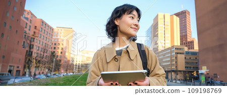 Happy young brunette girl, asian woman walks around city with tablet, goes to university with her digital gadget and backpack Happy young brunette girl, asian woman walks around city with tablet, goes to university with her digital gadget and backpack 109198769