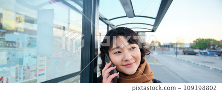 Close up portrait of cute young woman calling someone, waiting on bus stop with smartphone, using telephone while expecting public transport to arrive Close up portrait of cute young woman calling someone, waiting on bus stop with smartphone, using telephone while expecting public transport to arrive 109198802