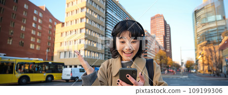Young happy woman celebrating on street, holding smartphone and cheering, reacts amazed to good news, reads phone text message with surprised joyful face 109199306
