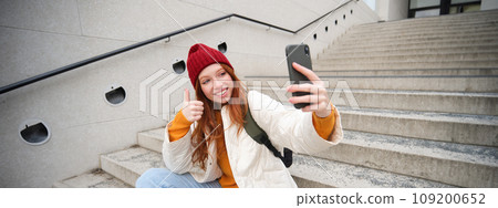 Urban girl takes selfie on street stairs, uses smartphone app to take photo of herself, poses for social media application Urban girl takes selfie on street stairs, uses smartphone app to take photo of herself, poses for social media application 109200652