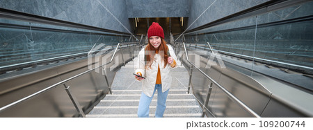 Outdoor shot of young woman plans route, follows map on smartphone app, goes up stairs with backpack and smiles Outdoor shot of young woman plans route, follows map on smartphone app, goes up stairs with backpack and smiles 109200744
