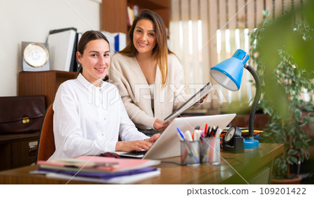 Woman assistant standing with documents near boss in office Woman assistant standing with documents near boss in office 109201422