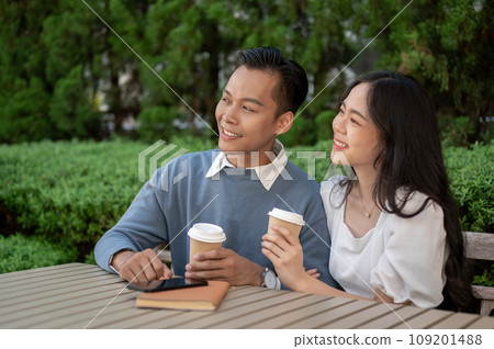 Young adorable Asian couple spending time together in the park, sitting close to each other. 109201488