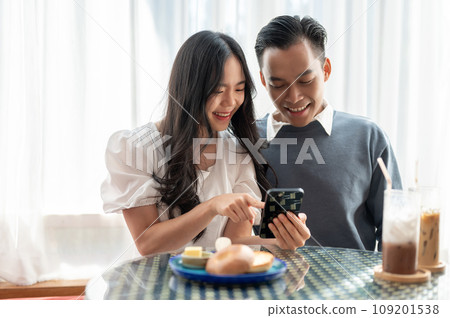 Young Asian couple having a date in a cafe, having good time together and playing with smartphone 109201538
