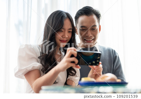 Young Asian couple having a date in a cafe, having good time together and playing with smartphone. 109201539