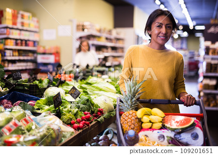 Satisfied hispanic woman with shopping trolley in supermarket 109201651