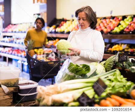 Elderly woman choosing cabbage in vegetable section of store Elderly woman choosing cabbage in vegetable section of store 109201654