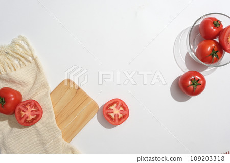 Scene for advertising with tomato ingredient. Fresh tomatoes and slices decorated with beige cloth, wooden tray and glass bowl on a white background. Top view, space to place your product 109203318