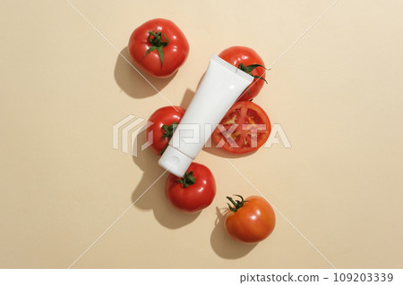 A white plastic bottle decorated with ripe tomatoes on a beige background. Mockup for cosmetic. Tomatoes contain compounds that help shrink pores, treat acne and brighten skin tone. 109203339