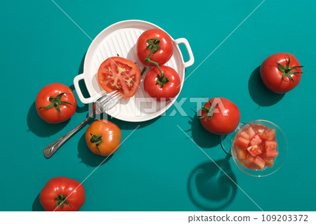 Minimal scene with fruit - top view of ripe fresh tomatoes with fork and white ceramic pan decorated on green background. Concept of natural ingredient for skin care and hair care 109203372