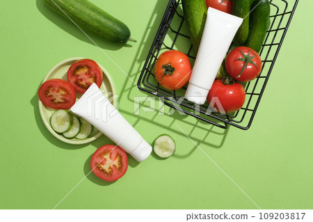 Two blank label tubes in white color displayed with a dish and a basket of tomatoes and cucumbers. Mockup of skin care cosmetic tube of beauty facial Two blank label tubes in white color displayed with a dish and a basket of tomatoes and cucumbers. Mockup of skin care cosmetic tube of beauty facial 109203817