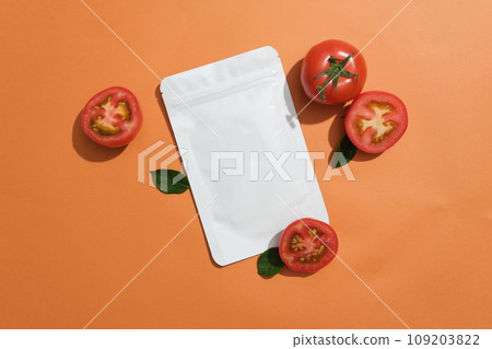 An unbranded facial mask package decorated with few halves of tomato over orange background. Natural cosmetic concept. Empty label for branding mockup An unbranded facial mask package decorated with few halves of tomato over orange background. Natural cosmetic concept. Empty label for branding mockup 109203822