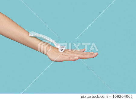 Precision in hand: A razor held against a striking blue backdrop, capturing the essence of grooming finesse Precision in hand: A razor held against a striking blue backdrop, capturing the essence of grooming finesse 109204065