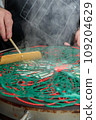 Preparation of colored pancakes. The cook's hands level the dough on the baking surface. Close-up 109204629