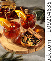 Tea with spices or mulled wine in a lined cup, with orange slices and cinnamon. On a wooden tray with tangerine and tea leaves in a bowl. Close-up.Winter content 109204635