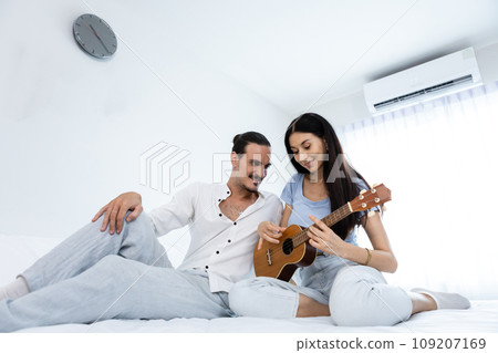 happy couple playing ukulele on bed in bedroom. happy couple playing ukulele on bed in bedroom. 109207169