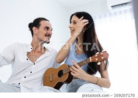 happy couple playing ukulele on bed in bedroom. happy couple playing ukulele on bed in bedroom. 109207170