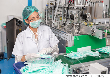 woman worker wear uniform are checking quality medical mask of manufacturer factory. 109207865