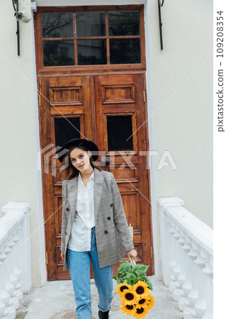 A woman in a hat with flowers on a walk near the front door 109208354