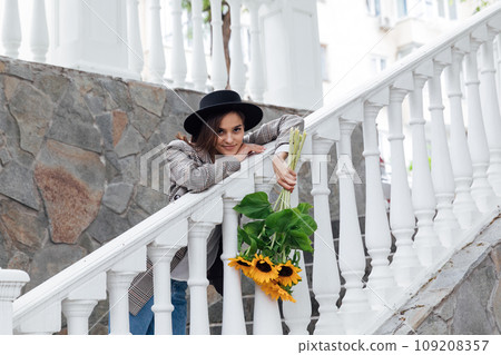 Woman in a hat with flowers on a walk near the railing Woman in a hat with flowers on a walk near the railing 109208357