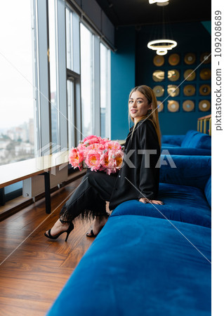 Female content employee sits on couch with bouquet of flowers Female content employee sits on couch with bouquet of flowers 109208689